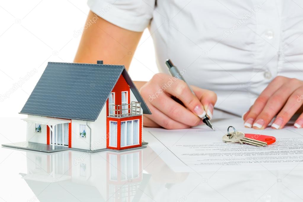A person signing documents related to estate and legacy planning, with a model house and keys on the table.