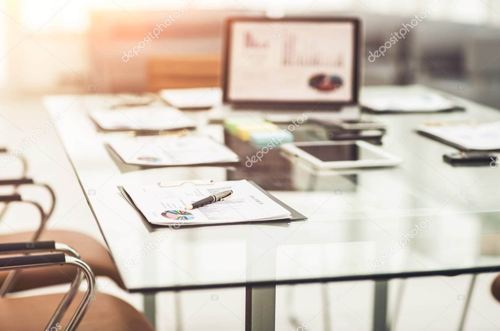 Business meeting with financial documents and laptop on a glass table.
