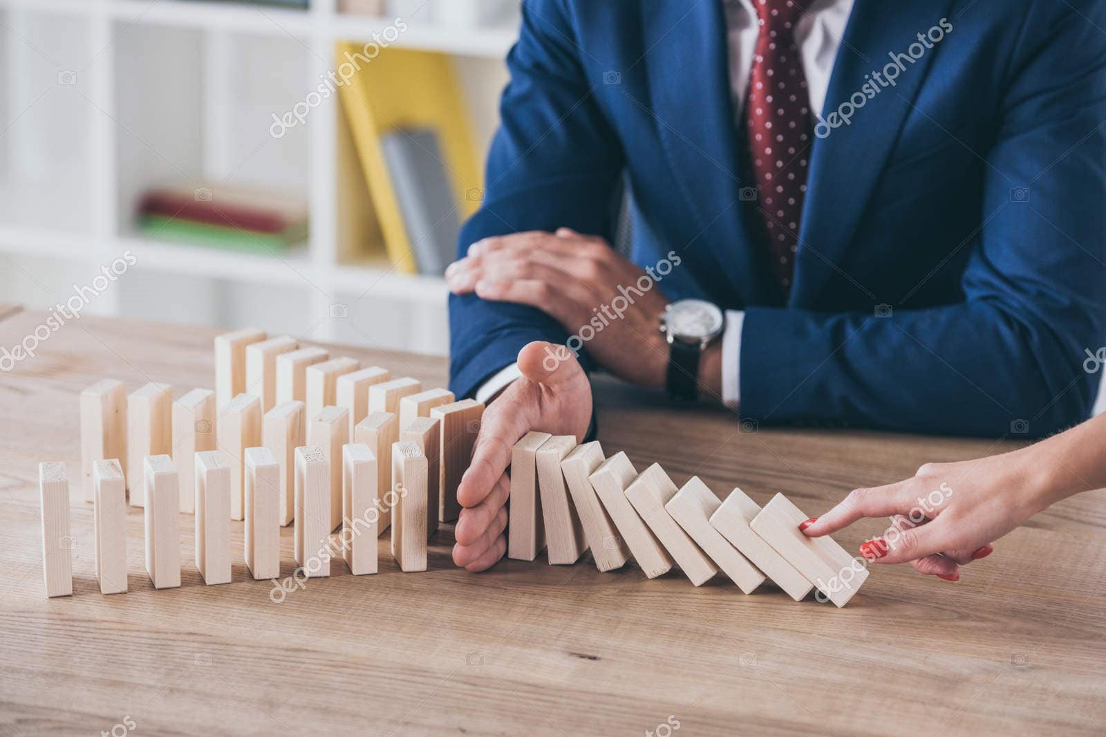 Businessman stopping dominoes from falling, symbolizing risk control.